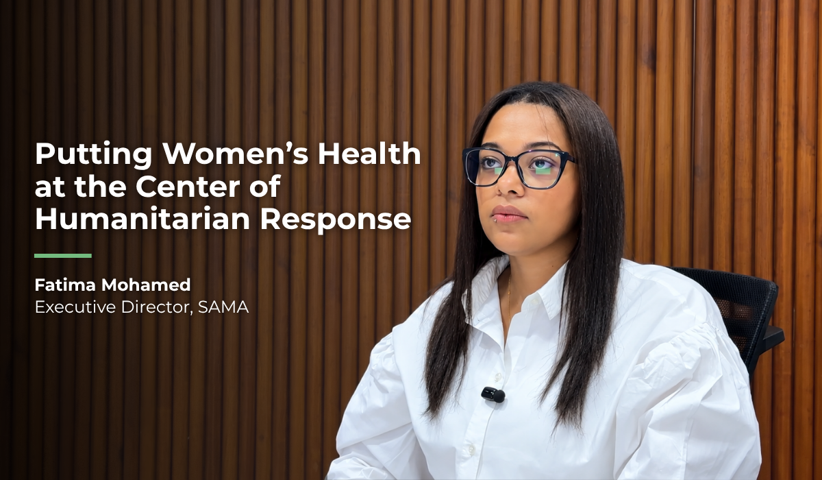 Fatima Mohamed, Executive Director of the Sudanese American Medical Association (SAMA), sits for an interview in front of a wooden panel background. Text reads: “Putting Women’s Health at the Center of Humanitarian Response — Fatima Mohamed, Executive Director, SAMA.”